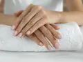 Dłonie z idealnym, jasnoróżowym manicurem kombinowanym spoczywają na białym ręczniku.