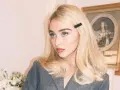 Blondynka z **side part fryzurą** i czarną spinką, w szarym żakiecie, z błękitnymi oczami.
