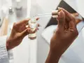 Dłonie trzymają buteleczkę z serum. Kropla z pipety, zawierająca kwas ferulowy, spada do buteleczki, przygotowując pielęgnację.