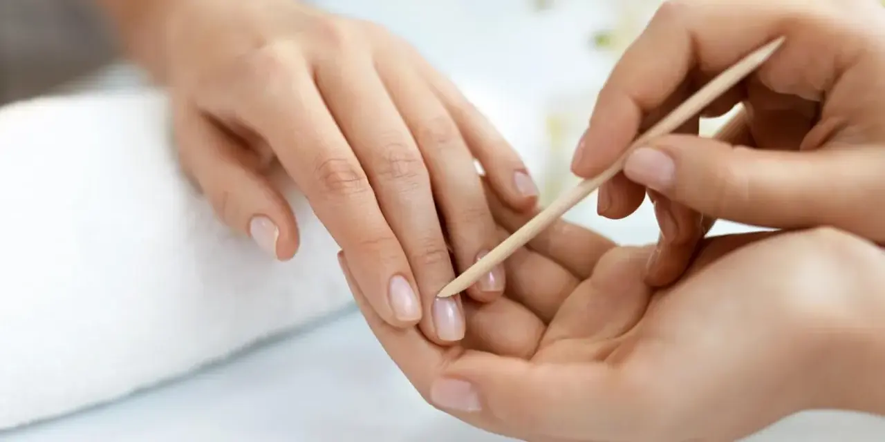 Delikatne dłonie poddawane zabiegowi manicure biologicznego. Skórki są starannie odsuwane patyczkiem.
