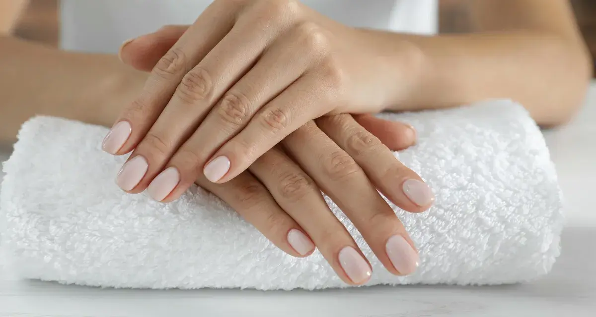 Dłonie z idealnym, jasnoróżowym manicurem kombinowanym spoczywają na białym ręczniku.