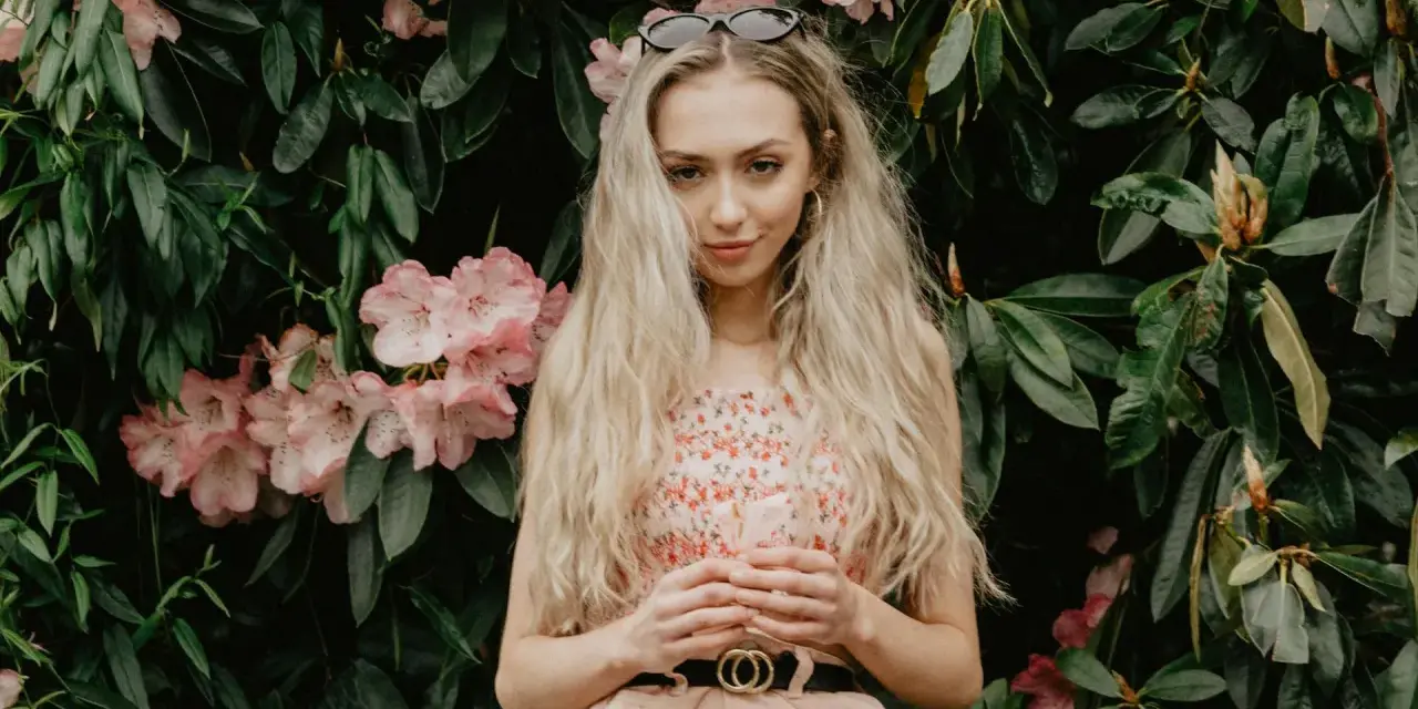 Blondynka w kwiecistej sukience, z okularami na głowie, otoczona różowymi kwiatami rododendronów. To kwintesencja słowiańskiej urody.