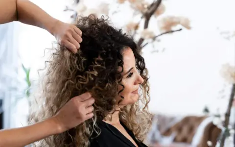Stylista układa kręcone włosy klientki, przygotowując się do strzyżenia. Wskazówki, jak obciąć kręcone włosy, pomogą uzyskać idealny kształt.