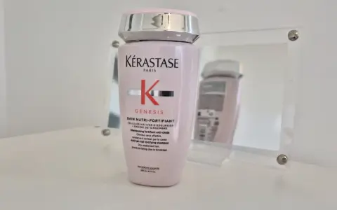 Różowa butelka szamponu Kérastase Genesis, odbijająca się w lustrze.