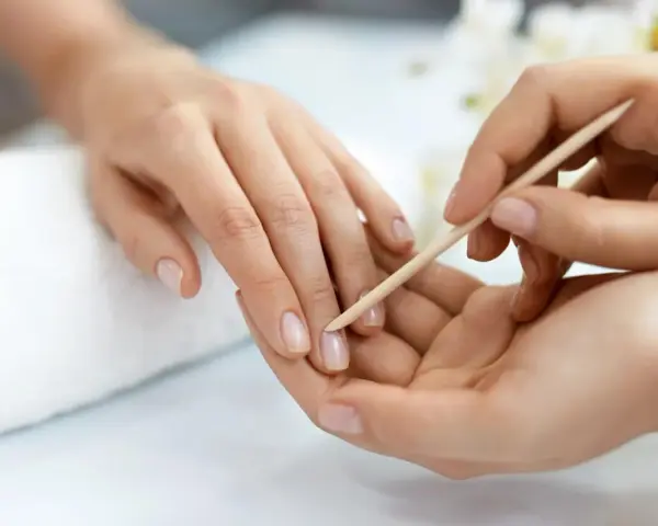Delikatne dłonie poddawane zabiegowi manicure biologicznego. Skórki są starannie odsuwane patyczkiem.