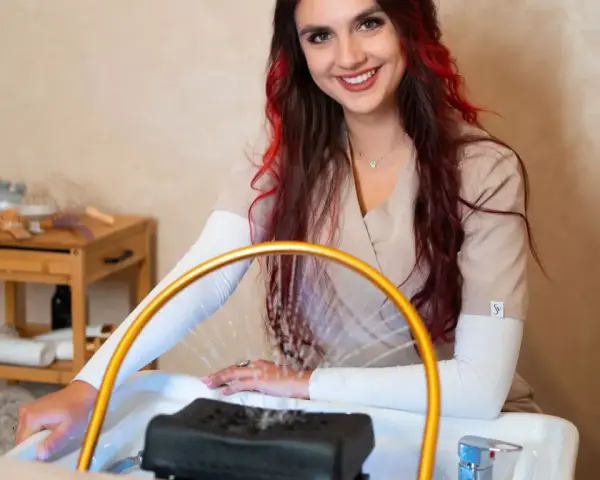 Uśmiechnięta stylistka z rudymi pasemkami przygotowuje się do zabiegu. Dowiedz się, ile kosztuje pedicure w tym salonie.