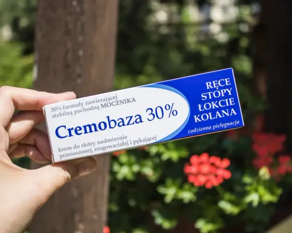 Dłoń trzyma opakowanie kremu Cremobaza 30%, przeznaczonego do pielęgnacji suchej, zrogowaciałej skóry dłoni, stóp, łokci i kolan.