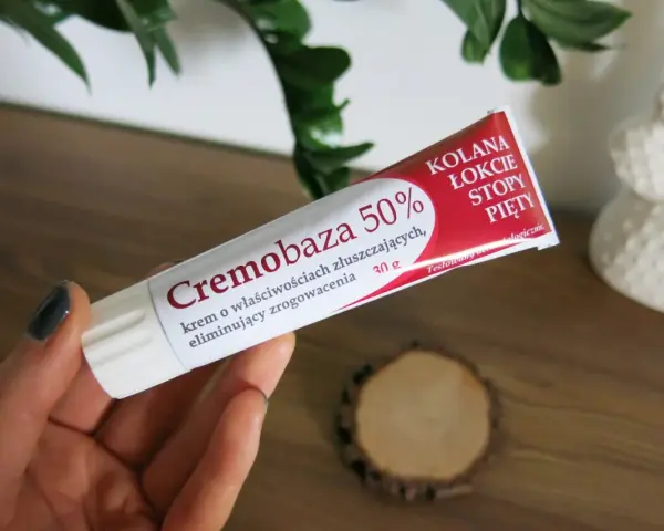 Dłoń trzyma tubkę kremu Cremobaza 50%, który pomaga na zrogowacenia. Brak informacji o skutkach ubocznych.