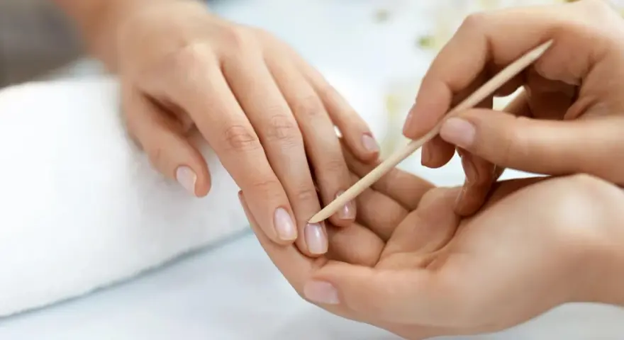 Delikatne dłonie poddawane zabiegowi manicure biologicznego. Skórki są starannie odsuwane patyczkiem.