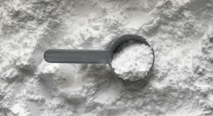 Miarka z białym proszkiem, prawdopodobnie disodium edta, na tle sypkiego materiału.