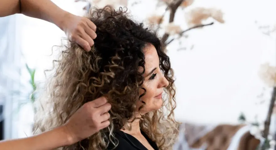 Stylista układa kręcone włosy klientki, przygotowując się do strzyżenia. Wskazówki, jak obciąć kręcone włosy, pomogą uzyskać idealny kształt.