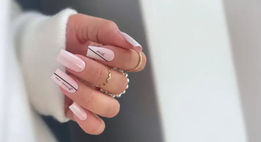 Delikatne, **milky nails** w odcieniach różu, ozdobione czarnymi napisami "smile" i "our moment".
