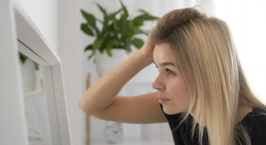 Kobieta z blond włosami sprawdza w lustrze, czy jej włosy są czyste po umyciu szamponem z **ammonium lauryl sulfate**.