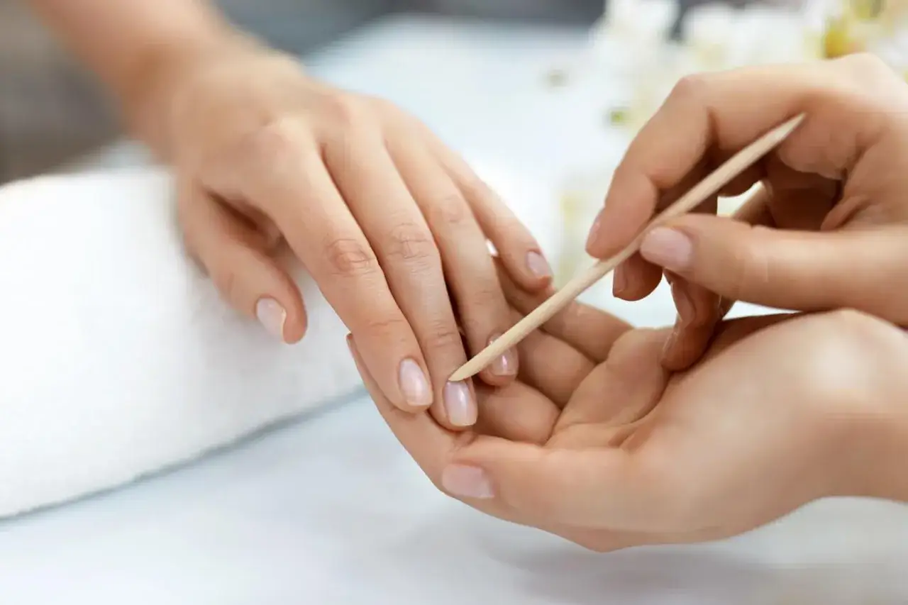 Delikatne dłonie poddawane zabiegowi manicure biologicznego. Skórki są starannie odsuwane patyczkiem.