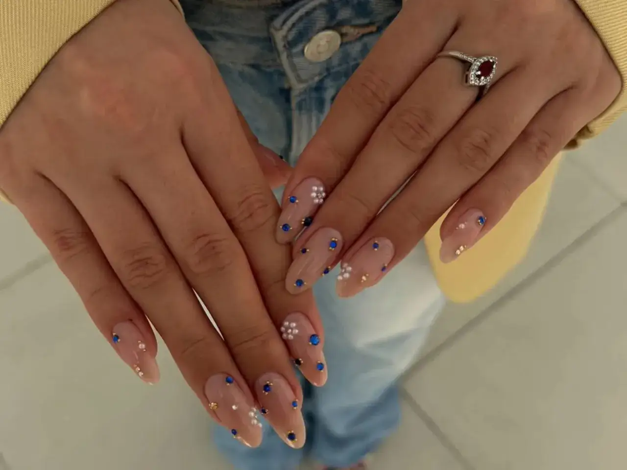 Eleganckie paznokcie w cielistym kolorze z białymi kwiatuszkami, granatowymi i złotymi drobinkami. Idealny pomysł na subtelny manicure.