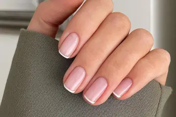 Dłoń z idealnie wykonanymi, modnymi paznokciami french. Delikatny róż i klasyczna biel tworzą ponadczasową elegancję.