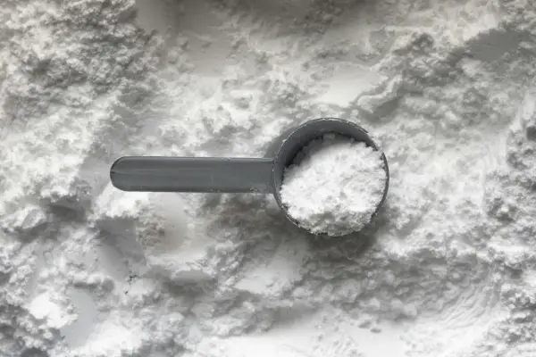 Miarka z białym proszkiem, prawdopodobnie disodium edta, na tle sypkiego materiału.